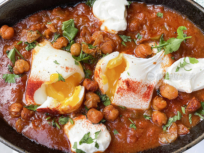 一锅地中海健康早餐的全画幅图片:shakshouka / shakshuka / chakchouka，鹰嘴豆，鸡蛋在番茄，辣椒，洋葱，橄榄油和大蒜的酱汁中水煮，顶部有香菜，高架视图